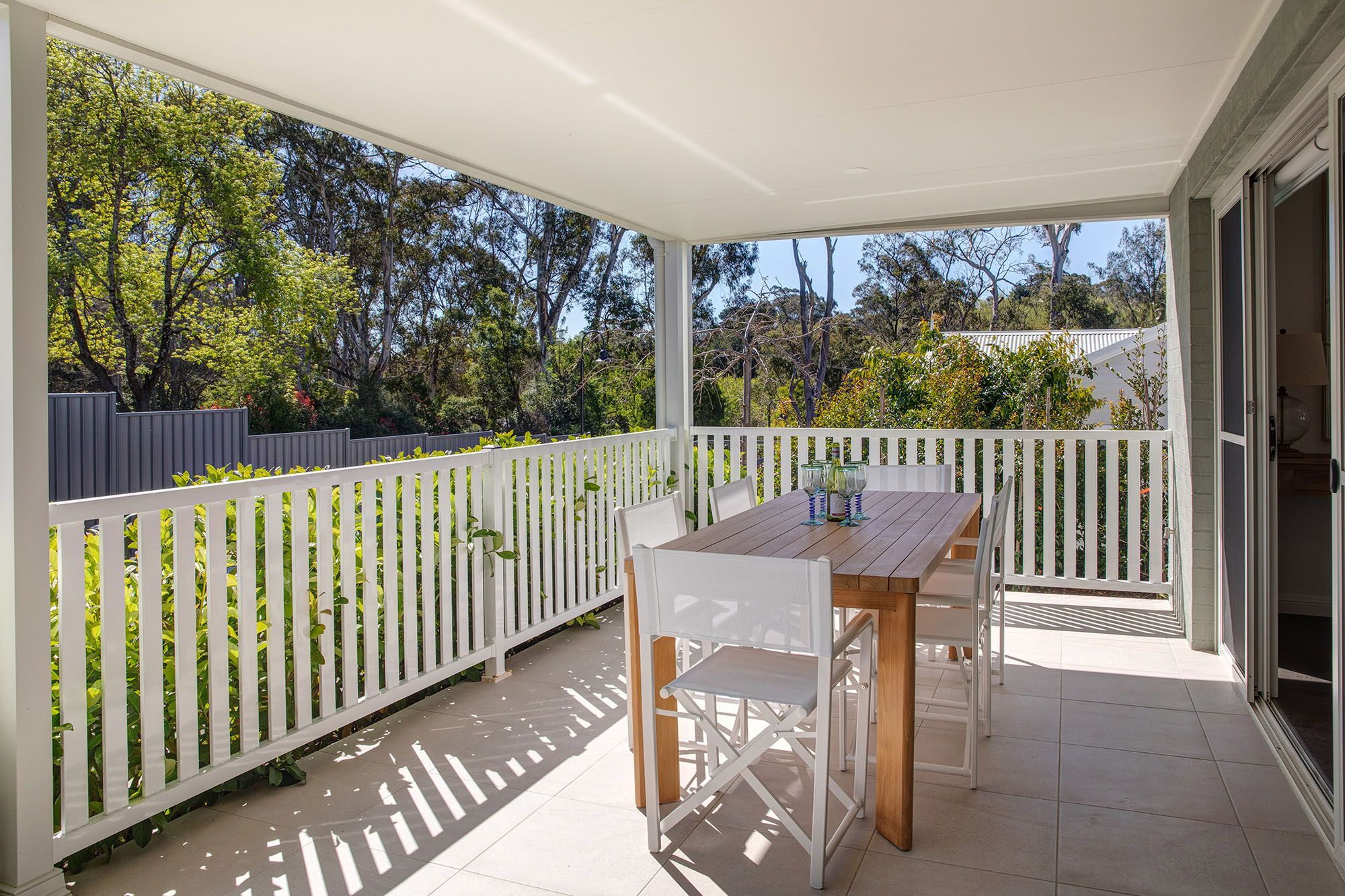 Covered outdoor deck with dining furniture, white balustrades and views of established gardens at Woodside Bundanoon.