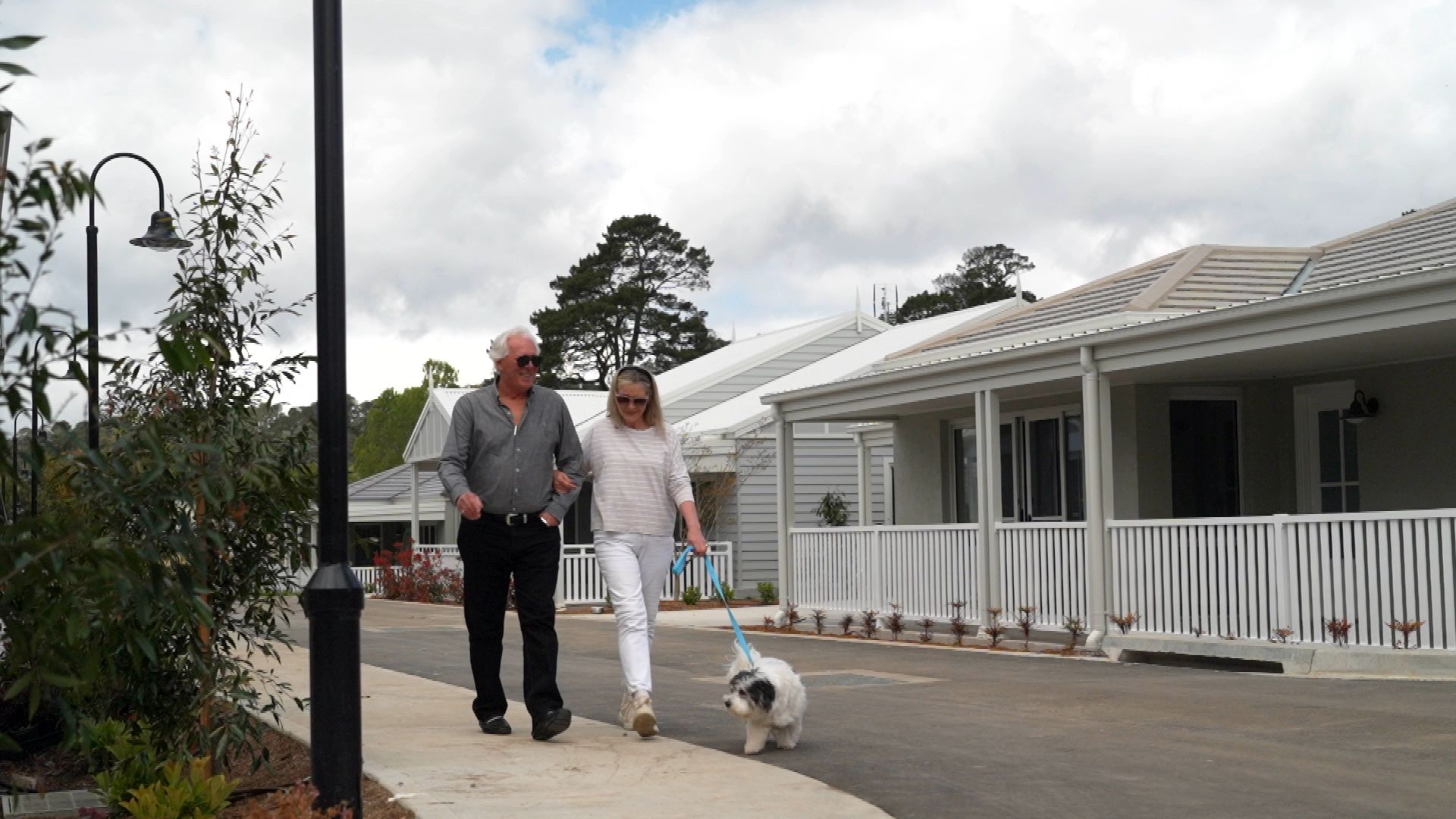 Couple walking their dog outside a freestanding, single-level home with a covered verandah at Woodside Bundanoon.